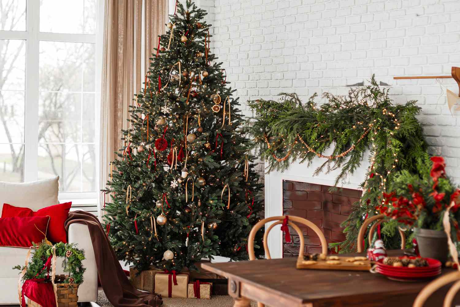 Christmas tree decorated with ornaments near a fireplace with garlands a festive dining table and living room setup