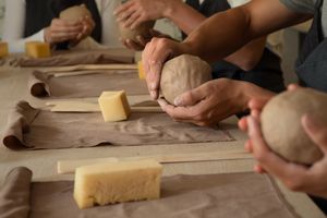 Hands shaping clay on a table, with materials and tools for pottery