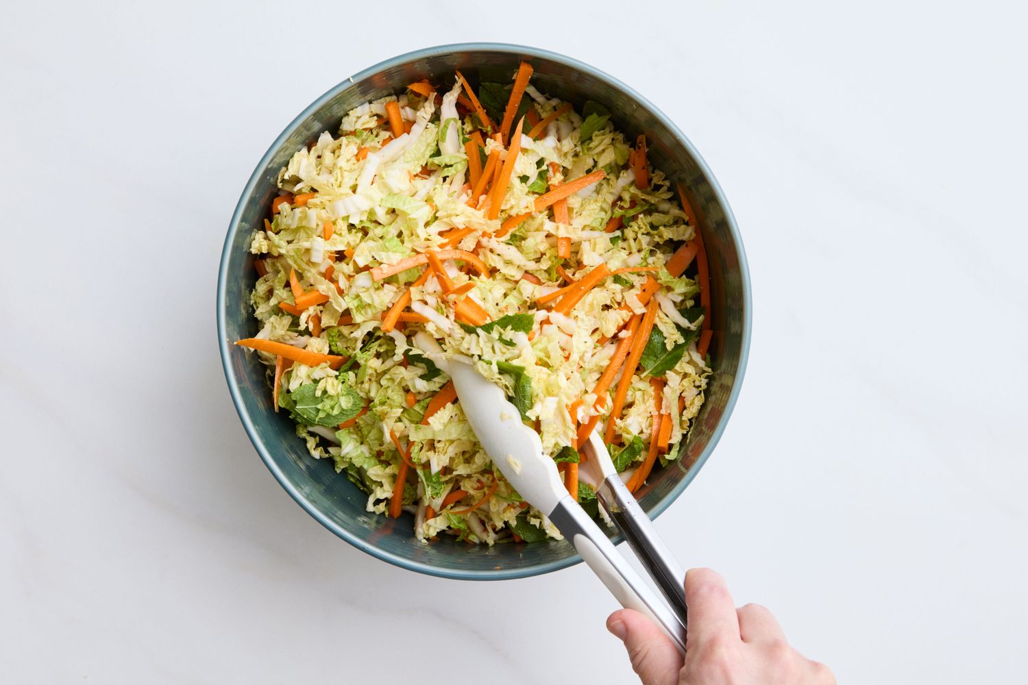 A bowl of napa cabbage slaw with carrots tongs placed inside