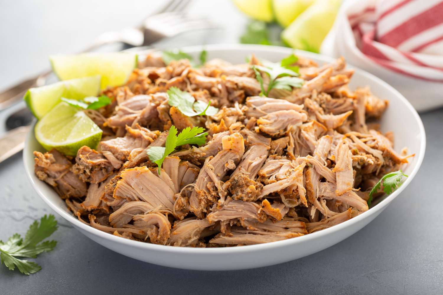 Pork carnitas in a bowl with celery and lime wedges. 