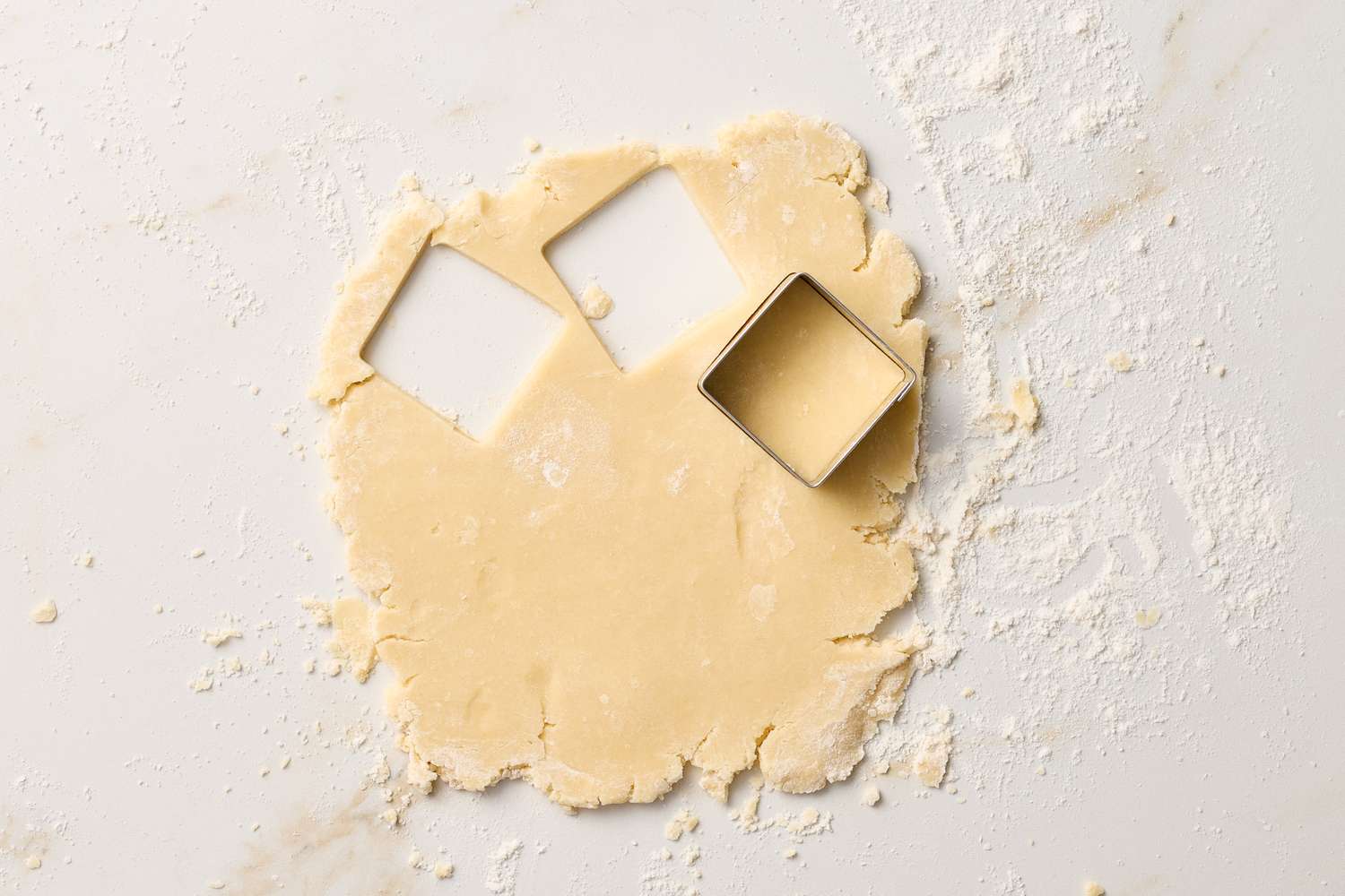 Rolled out cookie dough with a square cookie cutter cutting shapes