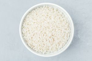A bowl filled with uncooked white rice on a gray surface