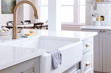 Farmhousestyle kitchen sink with a towel draped over the front surrounded by a bright kitchen with white countertops