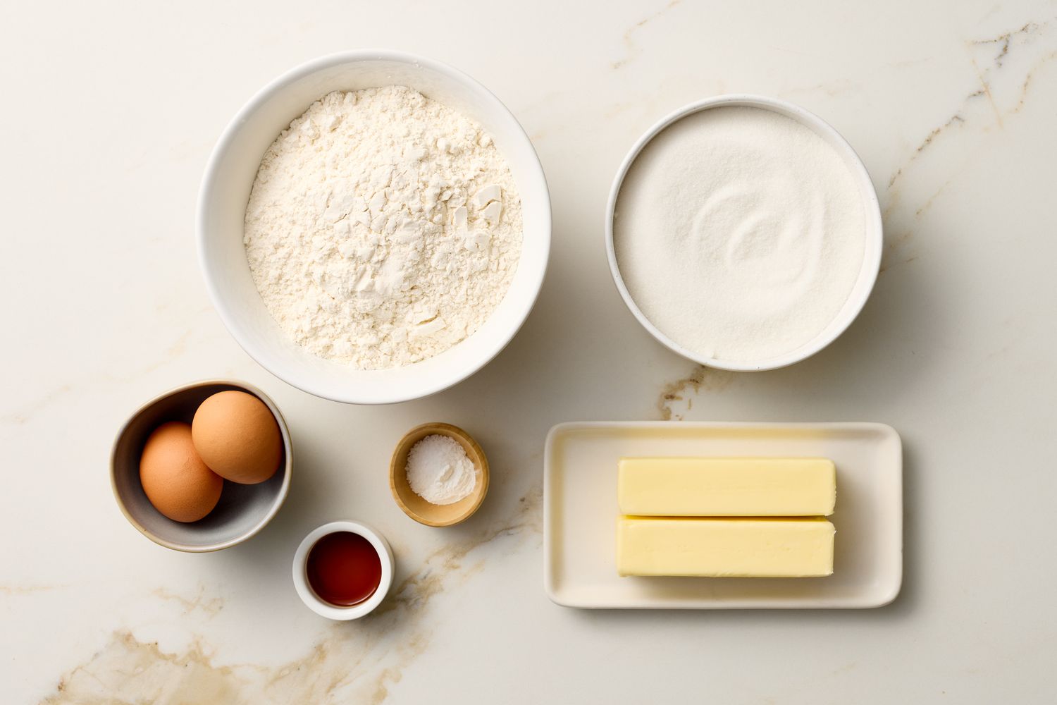 Ingredients for sugar cookies including flour sugar eggs butter vanilla and baking powder on a marble surface
