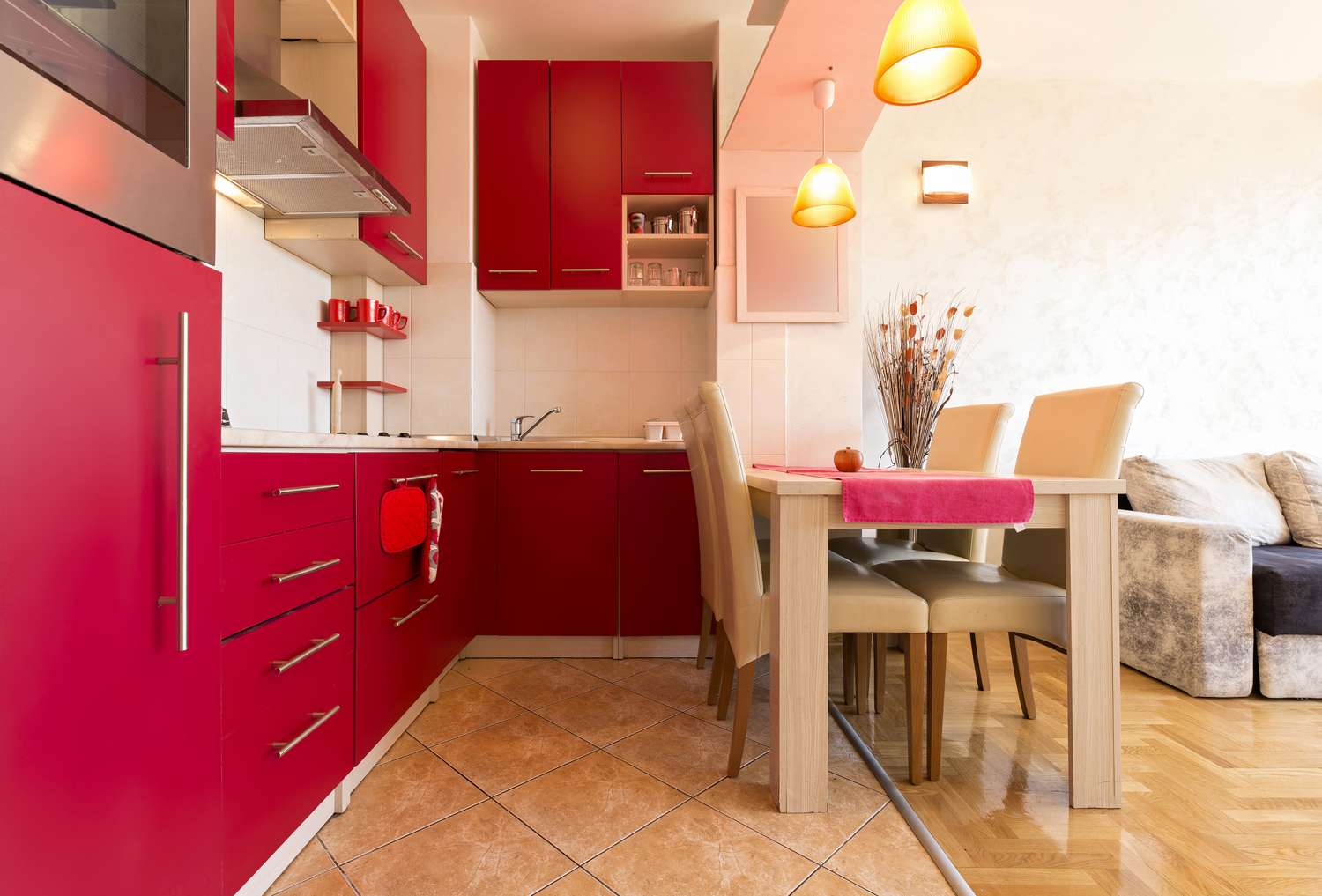 A modern kitchen with red cabinets and dining area with chairs and table