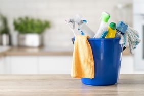 A blue bucket containing various cleaning supplies placed on a wooden counter in a kitchen setting
