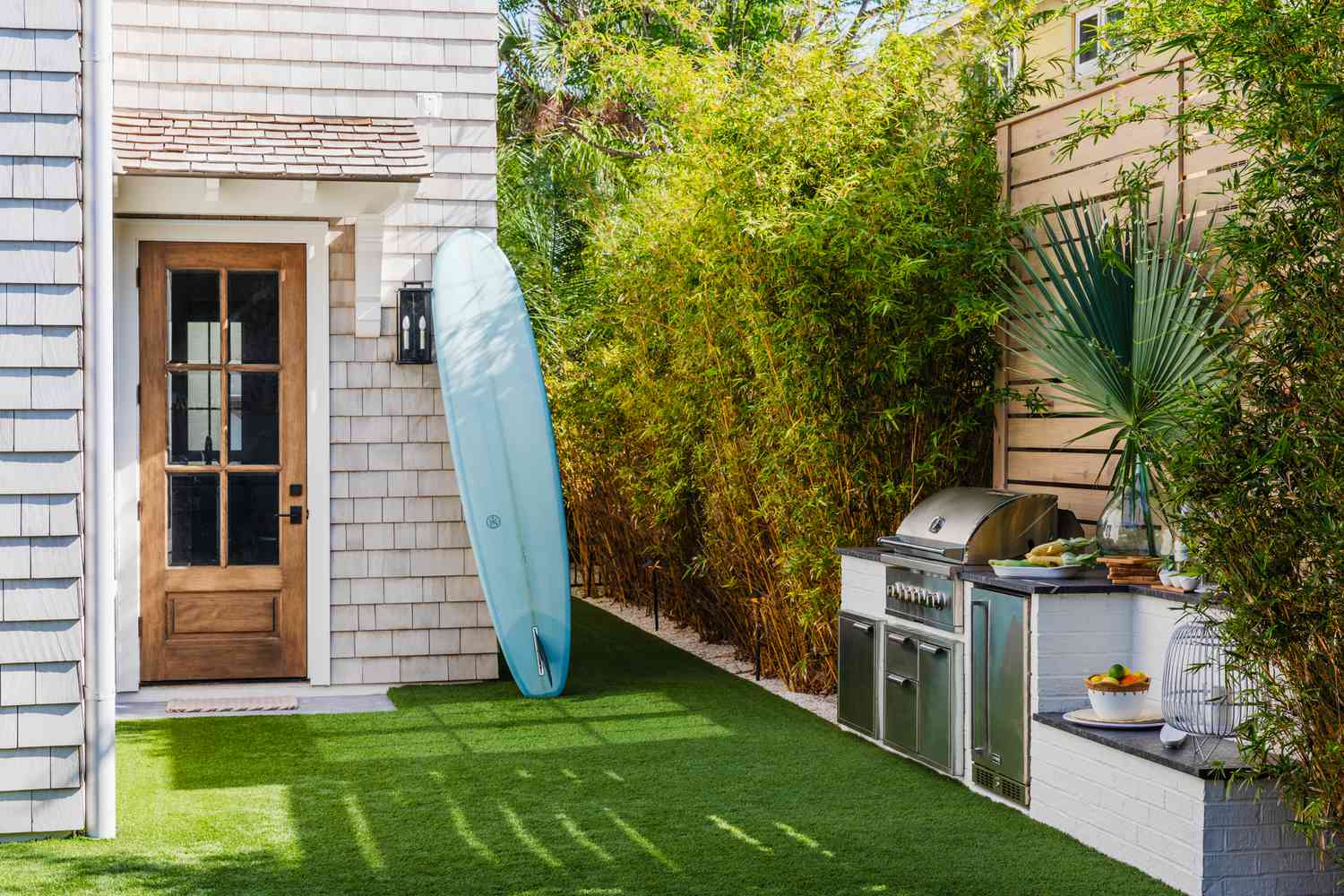 a turfed side yard with a compact white brick outdoor kitchen module built along the wooden fence