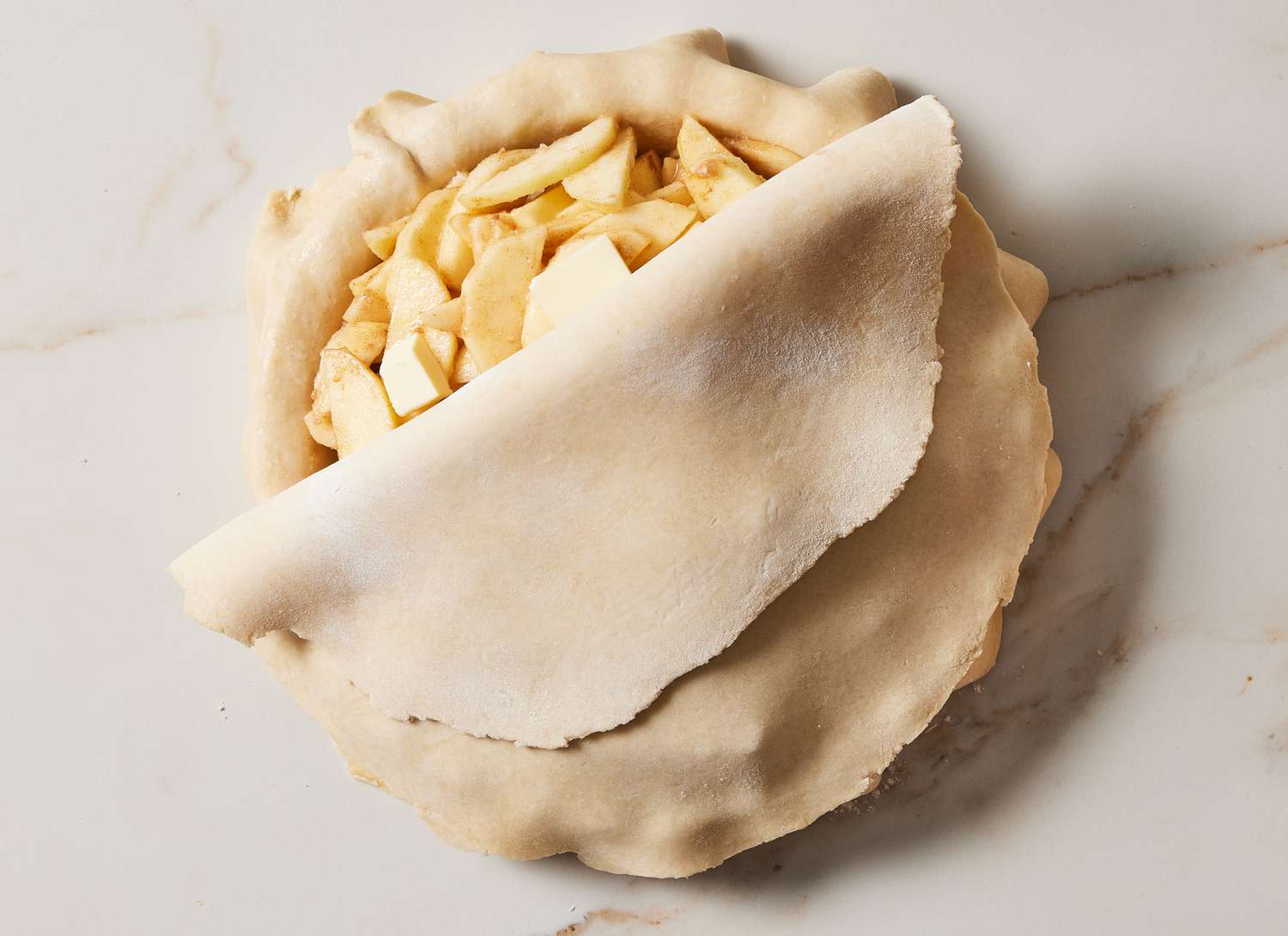 sliced apples in a pie crust with partially covered top layer of pie crust