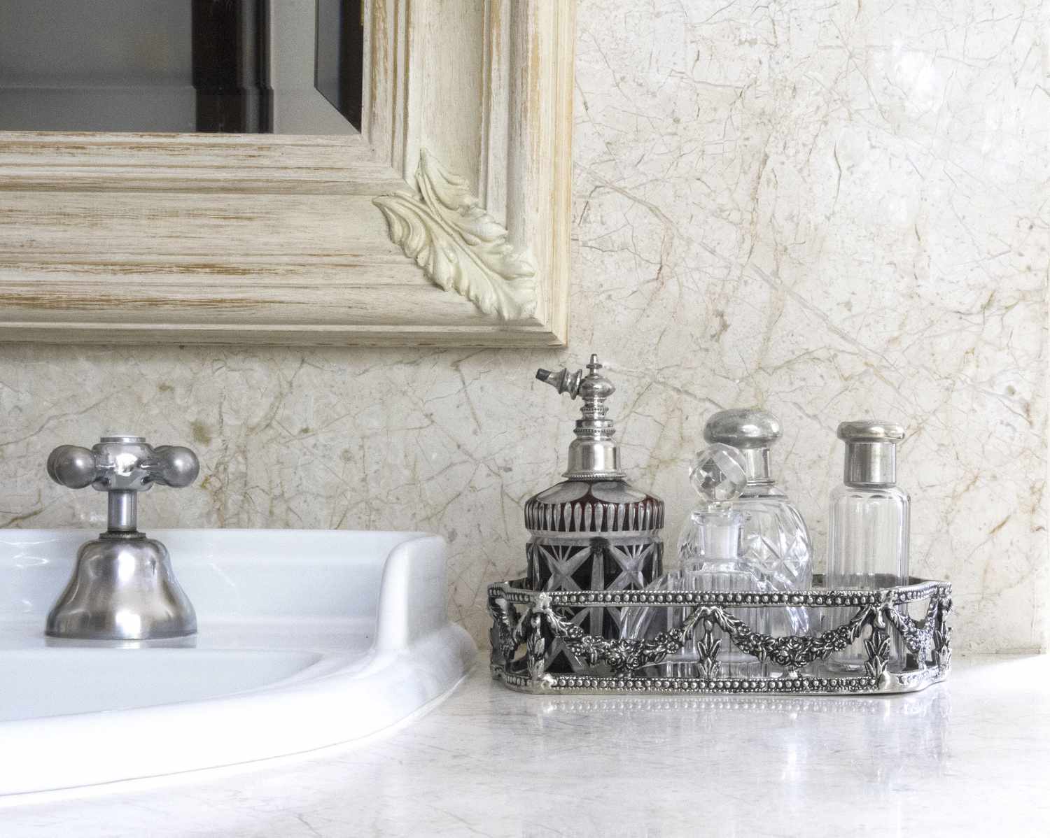 A bathroom countertop with decorative soap dispensers in an ornate caddy next to a sink and a framed mirror