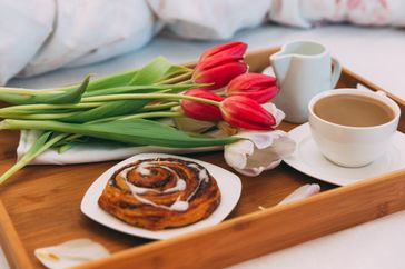 Breakfast tray with coffee a cinnamon roll tulips and a small pitcher of milk or cream