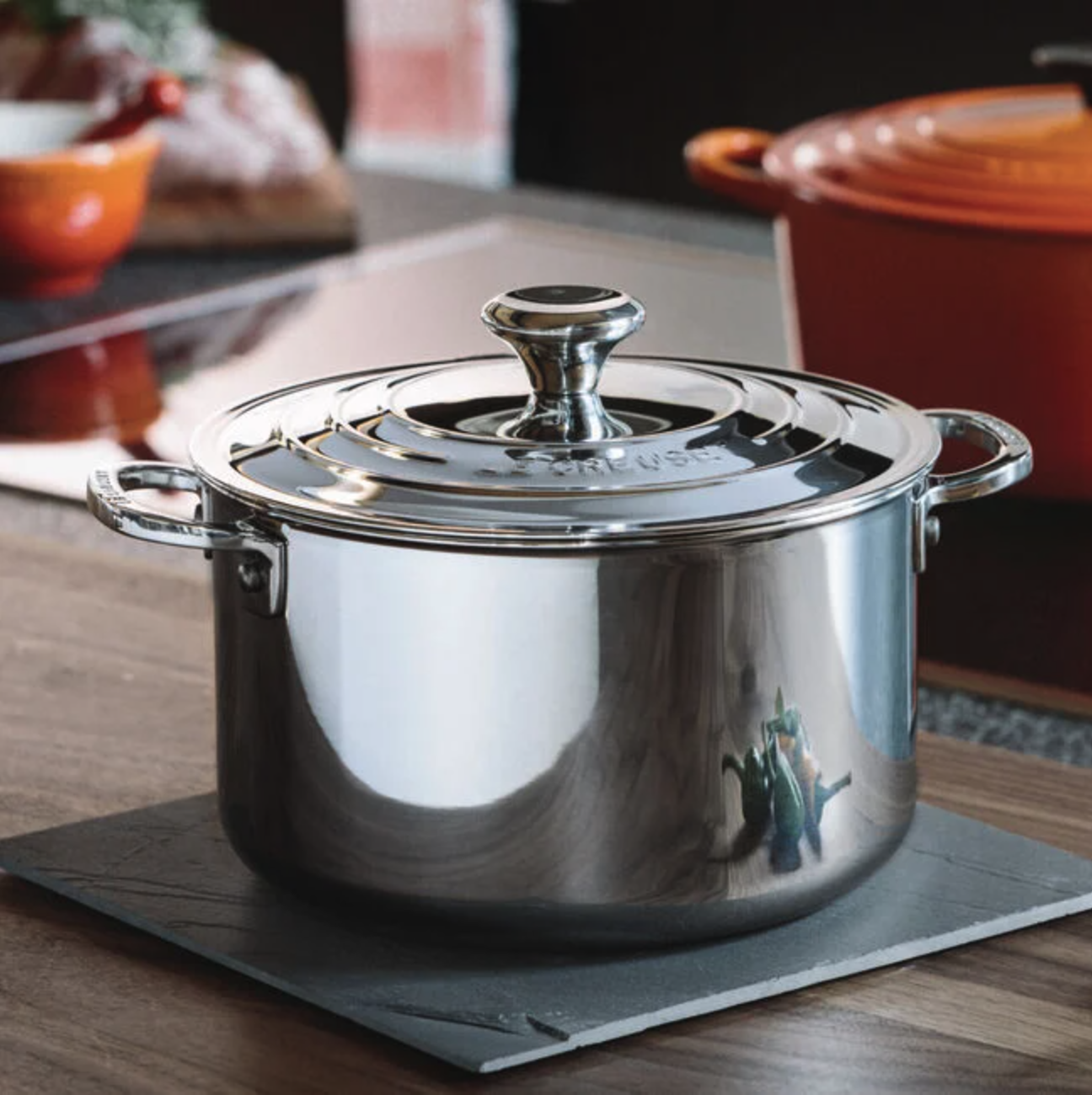 A stainless steel stockpot with a lid on a kitchen counter, another pot in the background