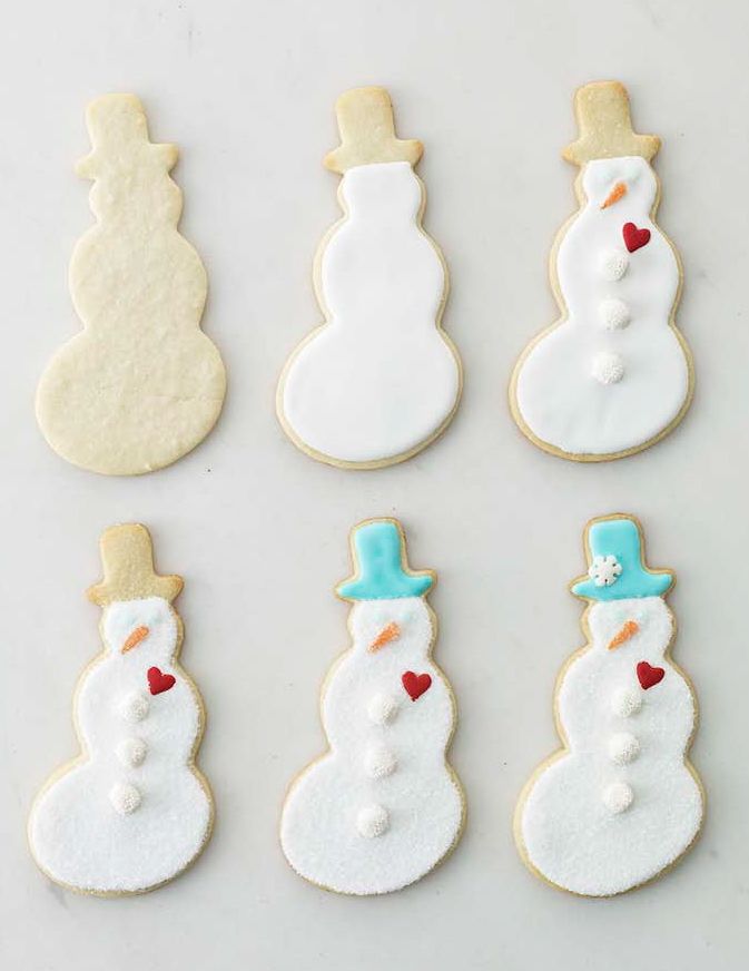 A set of six snowmanshaped cookies decorated in stages of completion on a flat surface showing progression from plain to fully decorated