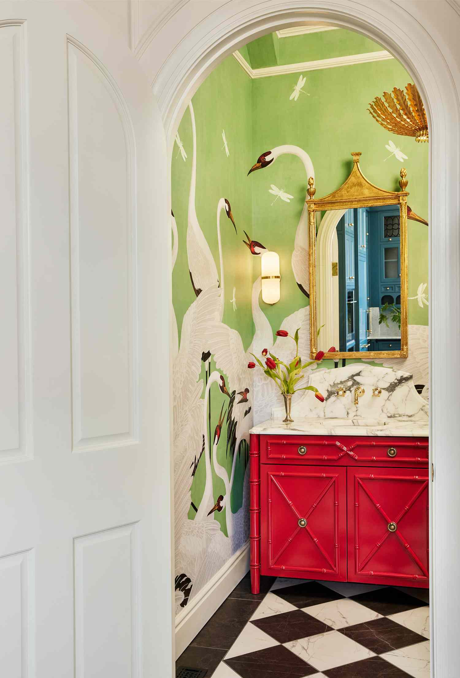 A decorated bathroom with swanthemed wallpaper a red vanity and ornate mirror visible through an arched doorway