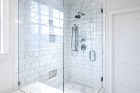 Modern glassenclosed shower with white tile walls and a rainfall showerhead