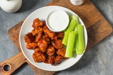 A plate with buffalo wings celery sticks and a cup of dipping sauce on a wooden board