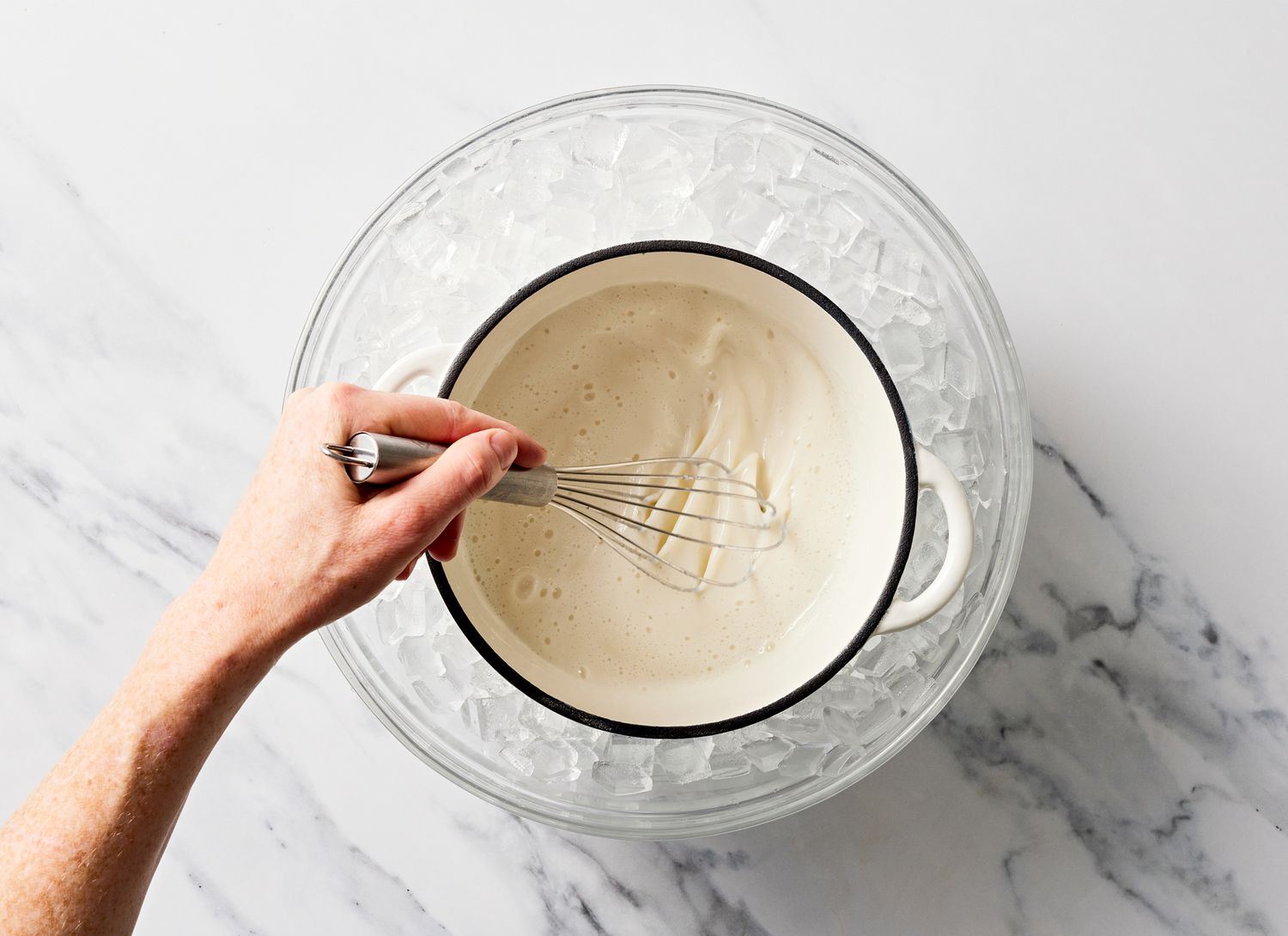 someone stirring white ingredients in a pot over a bowl of ice to cool