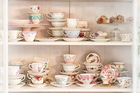 A display cabinet containing an assortment of teacups and saucers arranged on shelves
