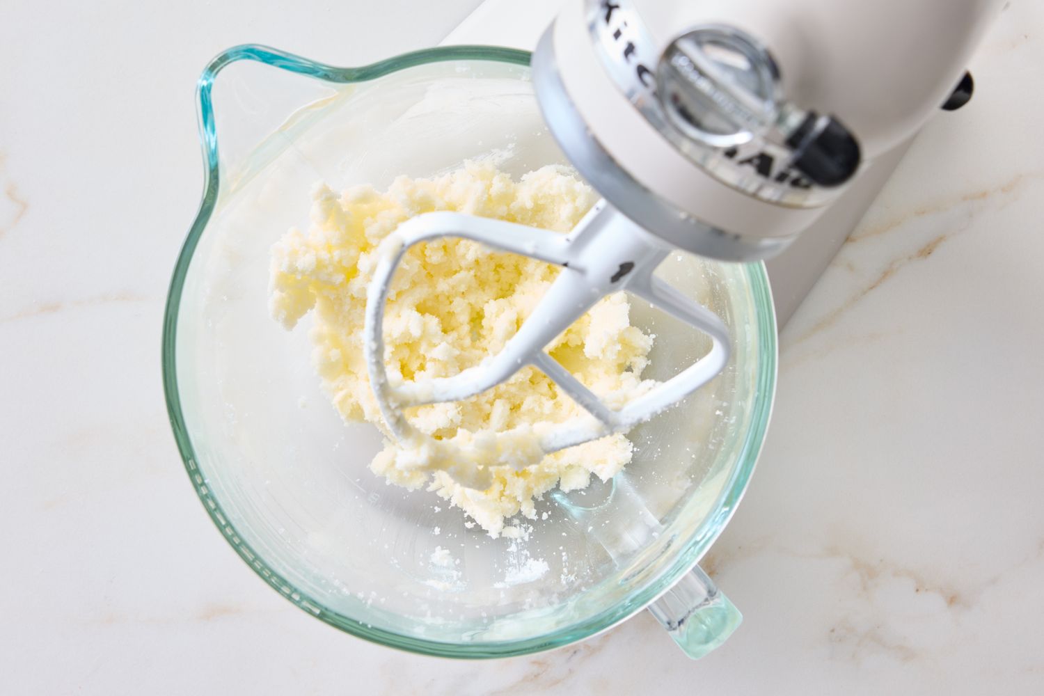 A stand mixer with a glass bowl containing creamed ingredients