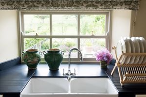 Kitchen sink with a window double sink with green decorative vases flowers and a dish rack on the counter