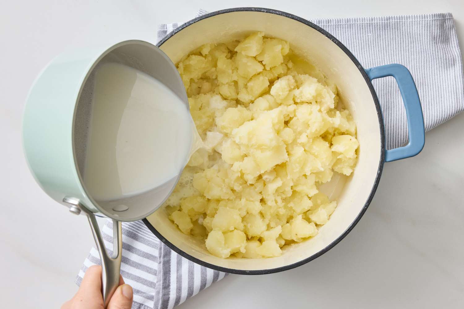 Mashed potatoes being prepared in a pot with milk being poured in