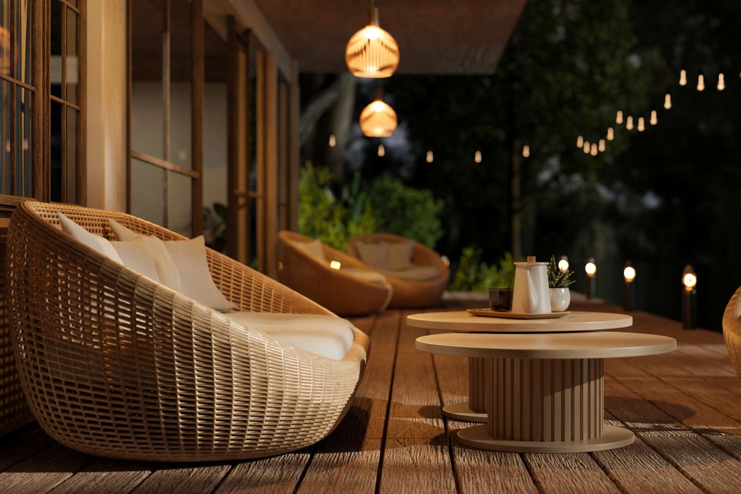 Outdoor patio area with wicker furniture round tables adorned with small decor and pendant lights hanging above surrounded by greenery
