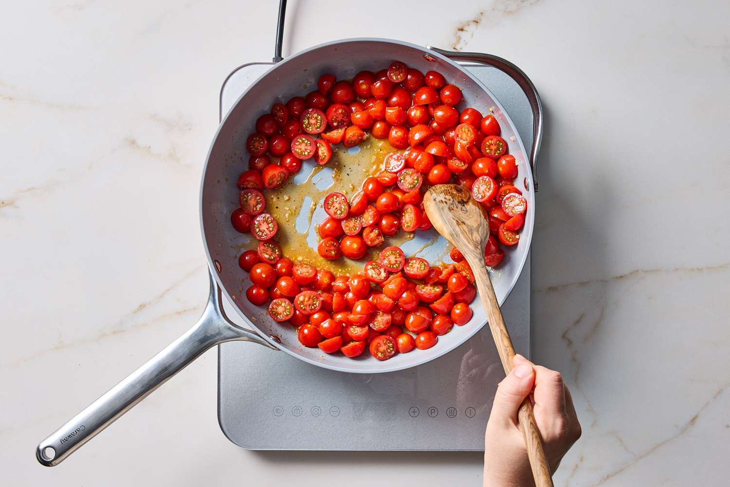 A skillet of sauted cherry tomatoes being stirred with a wooden spoon on a stovetop