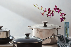 Cookware including pots and a pan displayed on a table with a striped fabric and an orchid branch in a vase