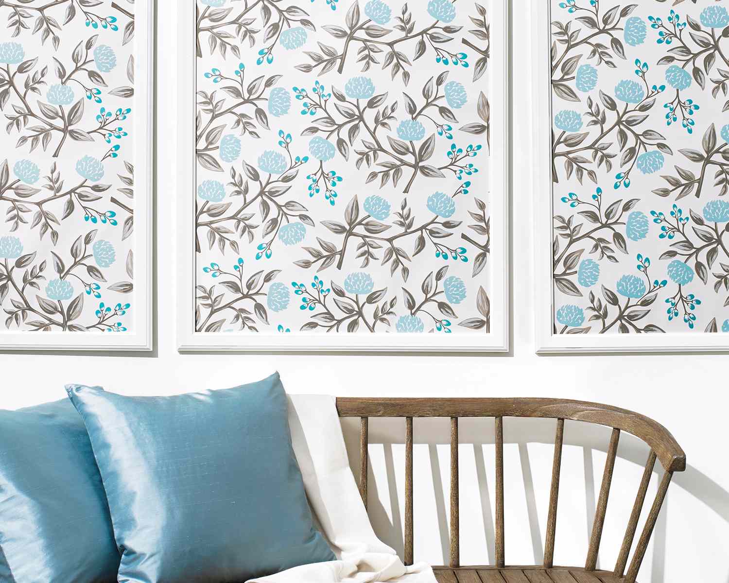 Three framed floral pattern artworks on a wall above a wooden bench with blue and white cushions