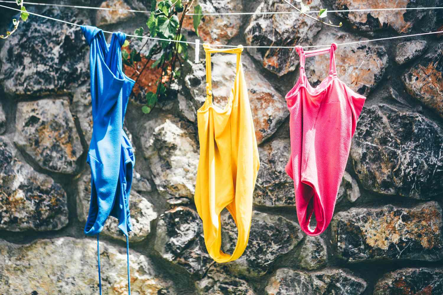 Three swimsuits hanging on a line in front of a stone wall