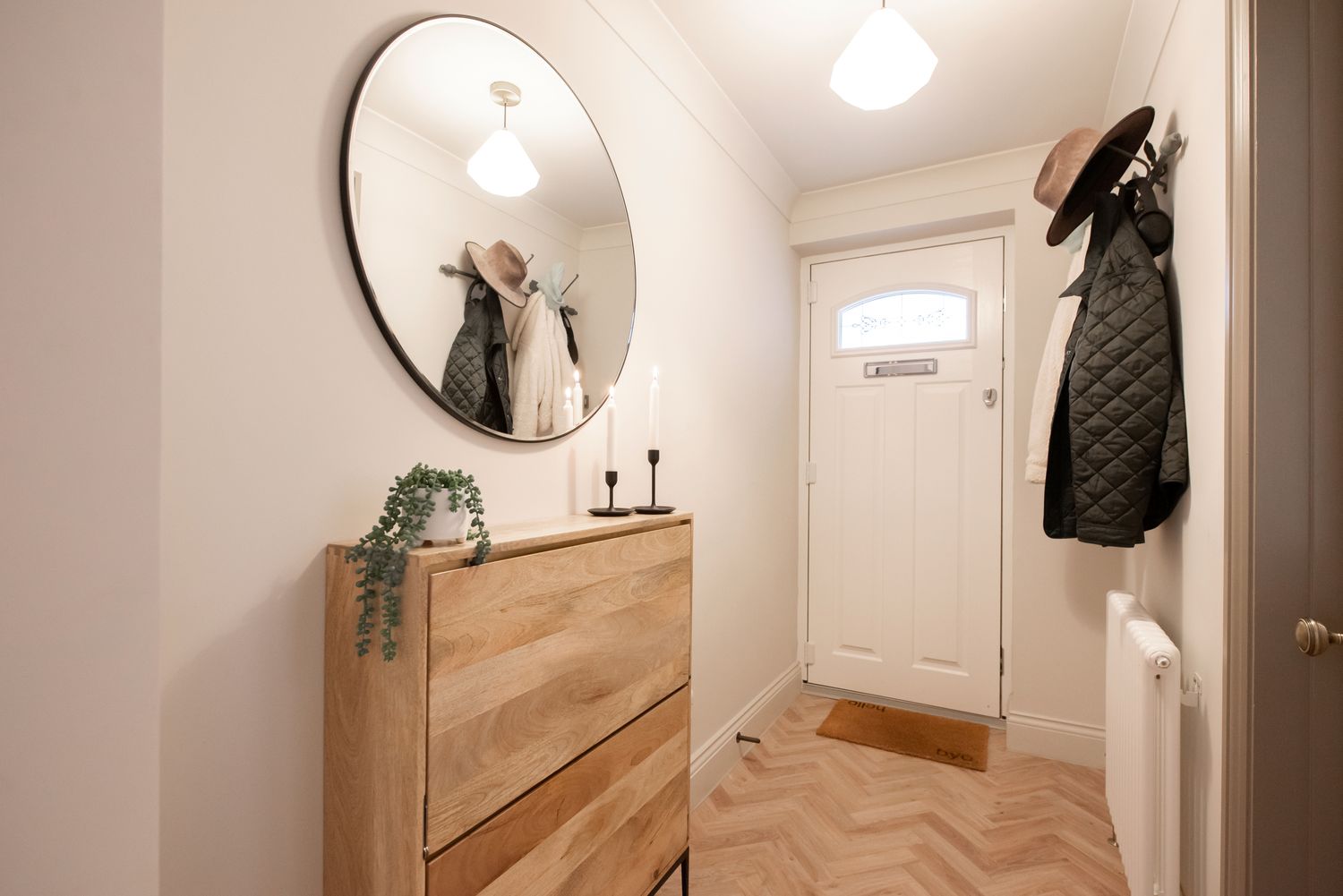 Home entryway with a round mirror above a wooden dresser a coat rack and a front door in view