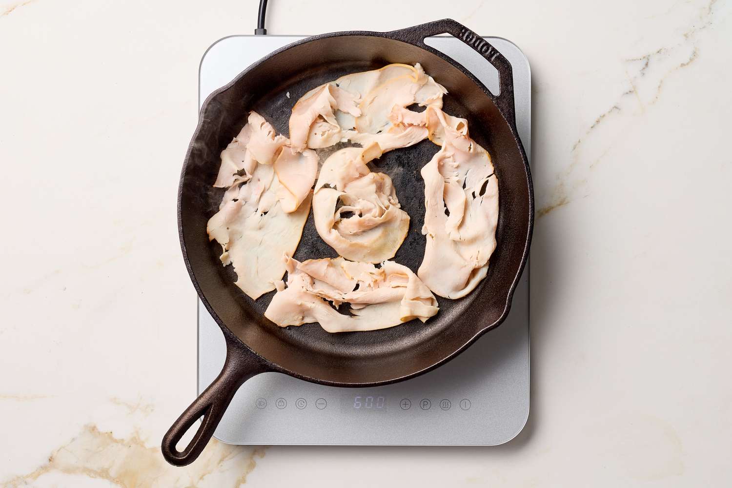 Slices of turkey cooking in a skillet on a cooktop