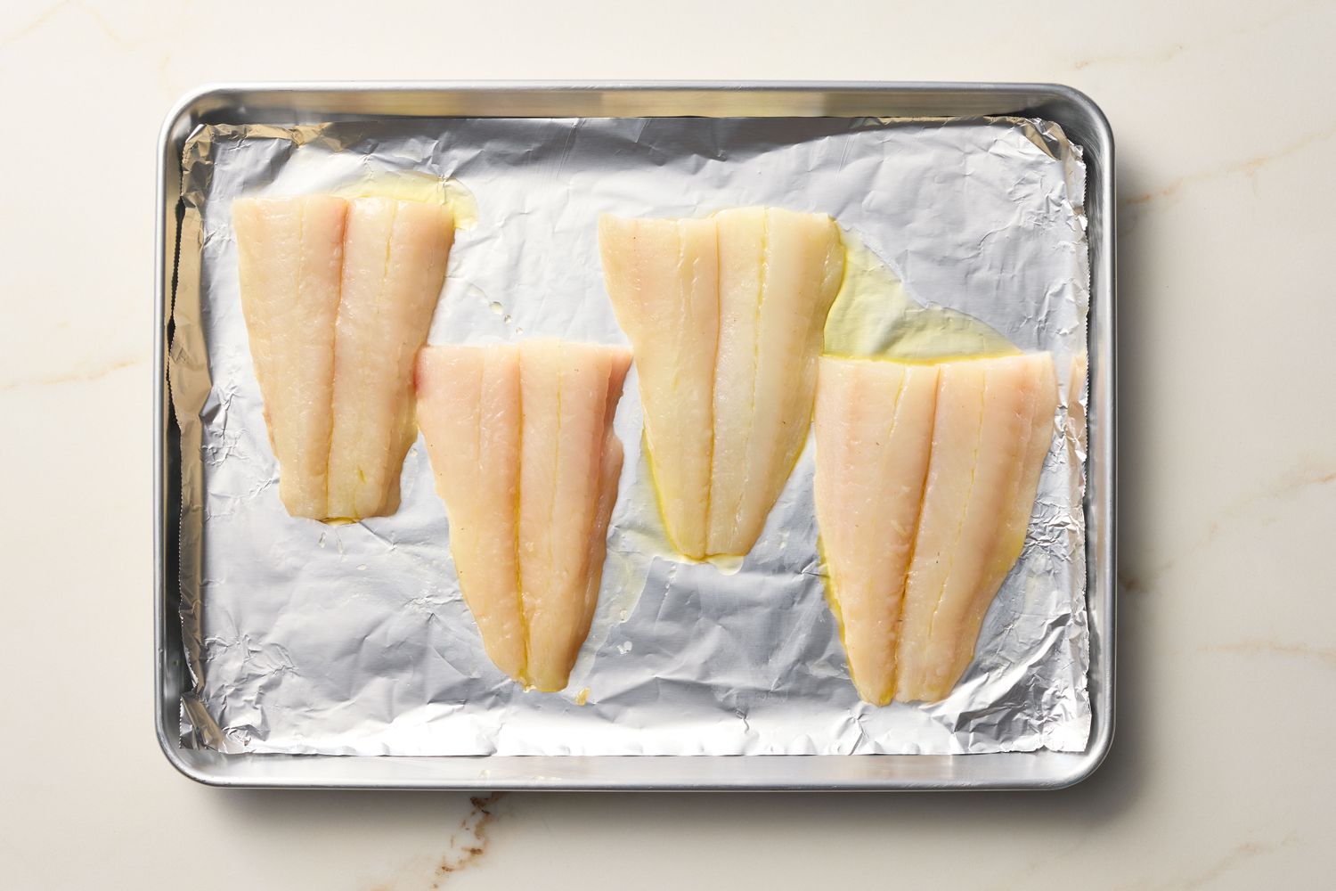 Four fish fillets placed on an aluminum foil-lined baking sheet