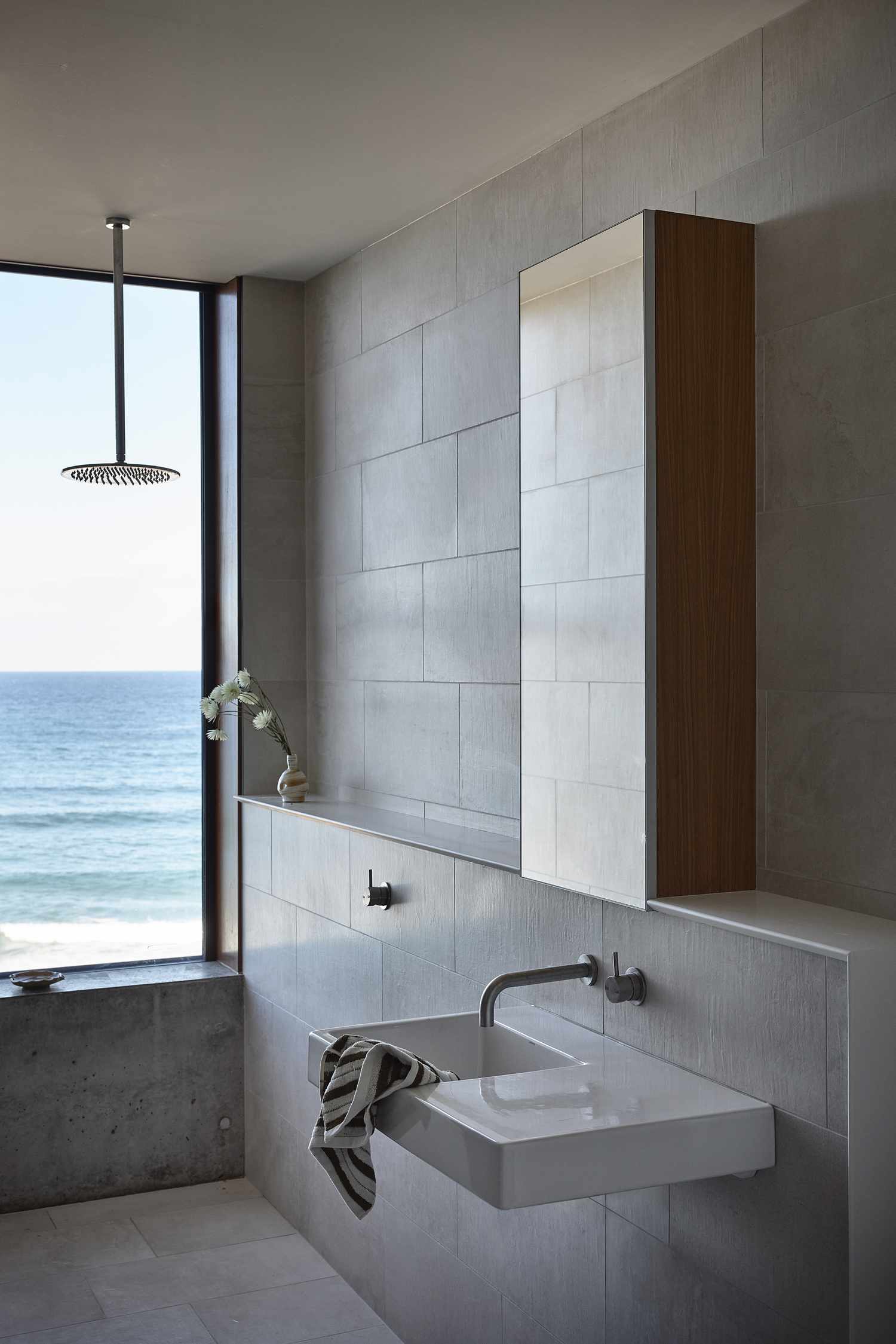 Minimalistic bathroom with large format tiles with a large window overlooking the ocean to bring the outdoors in.