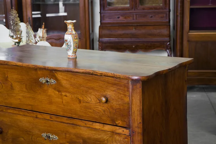 Antique wood dresser with ornate details and a decorative vase on top placed in a furniture showroom atmosphere