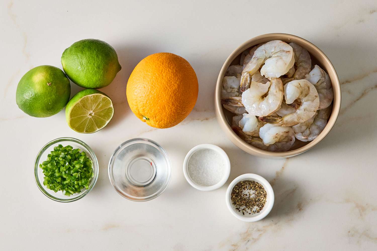 Ingredients for tequila grilled shrimp arranged on a surface including shrimp limes orange chopped herbs and small bowls of seasonings