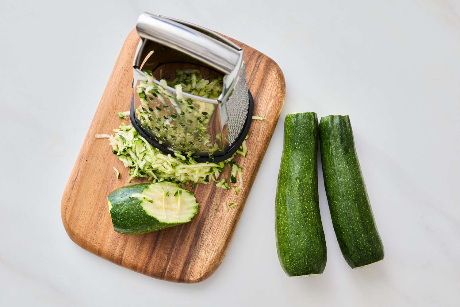 Zucchinis on a cutting board with a grater and shredded pieces