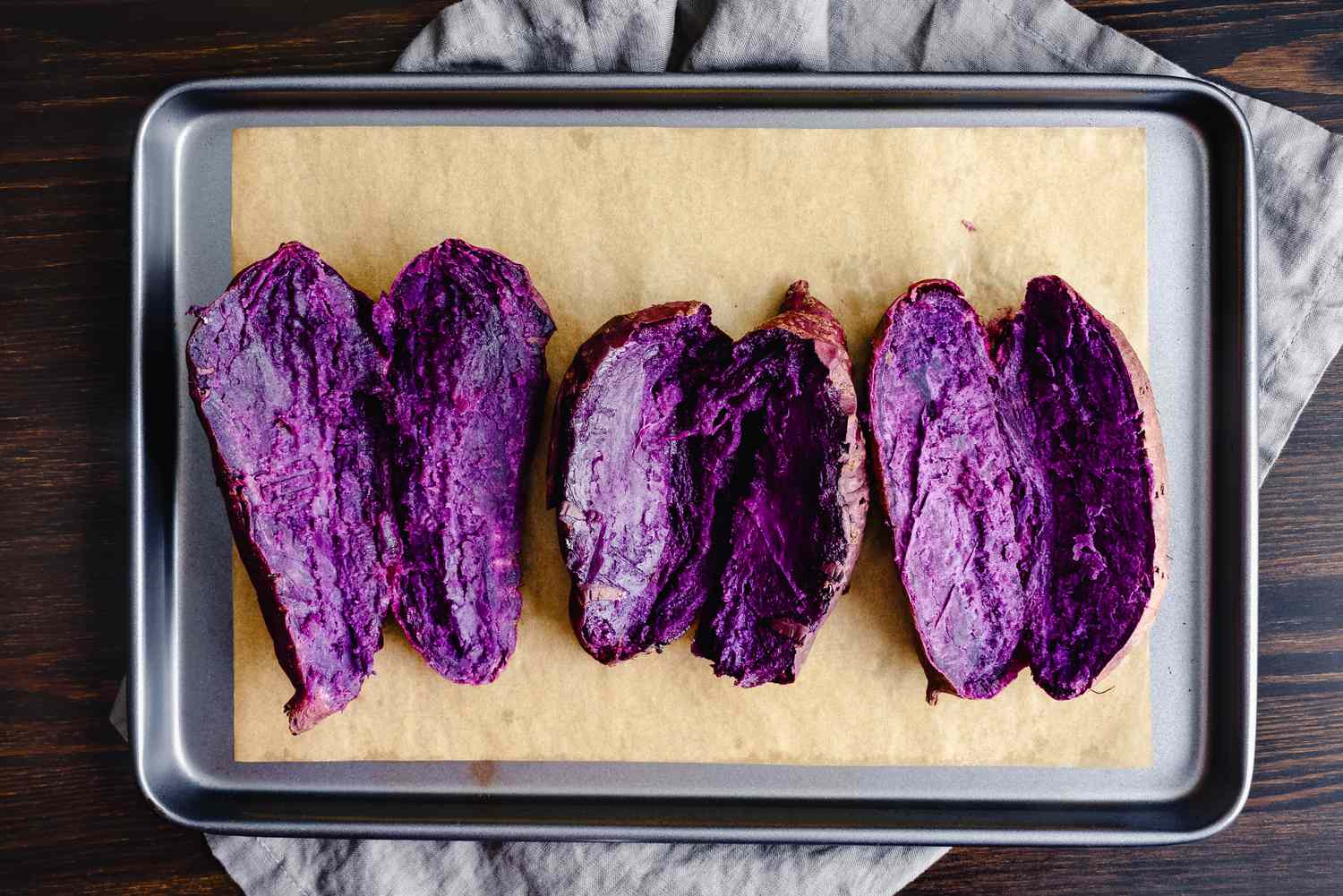 Halved purple sweet potatoes on a baking tray lined with parchment paper