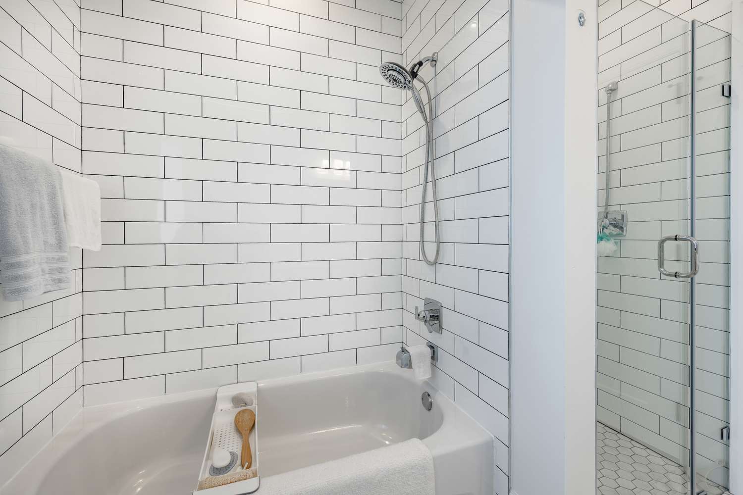 Bathroom with white tiled walls a bathtub with a wooden tray and a glass shower enclosure