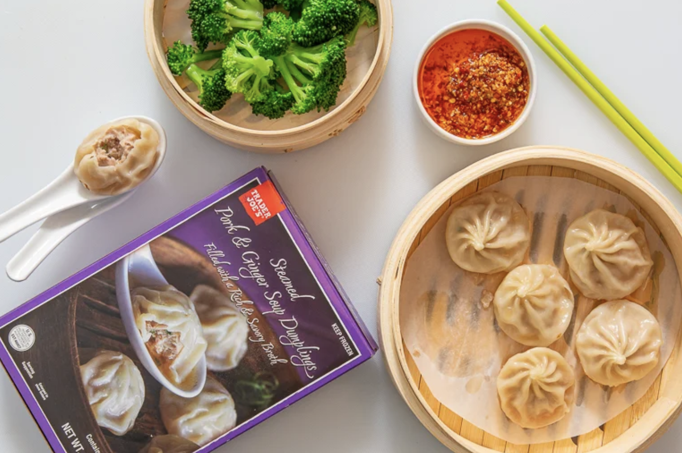 Pork and ginger soup dumplings in packaging with steamed dumplings broccoli and chili oil on a table