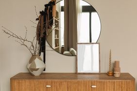 Wooden console with a decorative vase containing bare branches a round mirror and a framed item