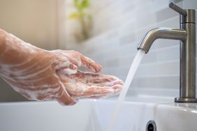 Hands being washed under running water from a faucet with soap lathered on the skin