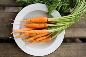 A plate of fresh carrots with greens on a wooden surface