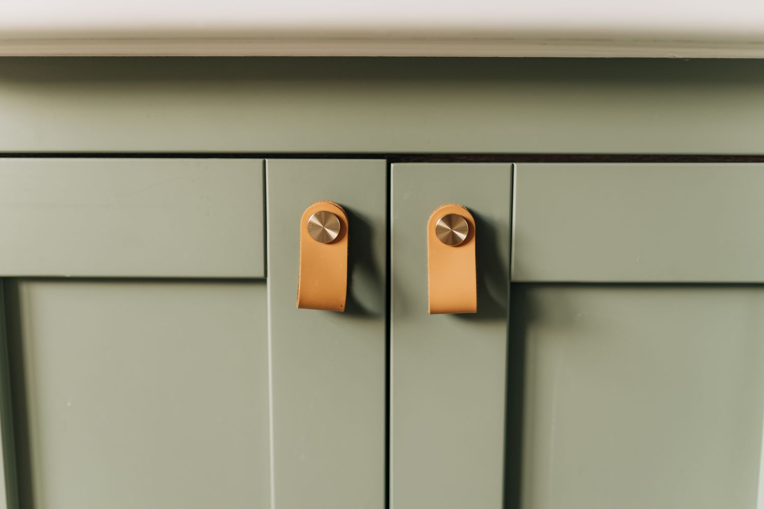 Closeup view of a cabinet with two leather pull handles featuring round metal fasteners