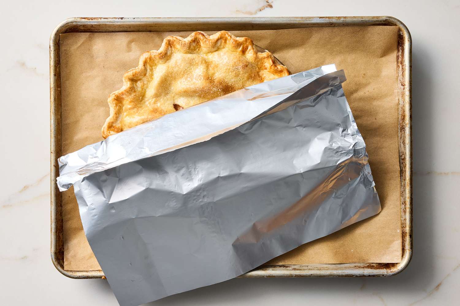 A baked pie partially covered with foil on a baking sheet with parchment paper
