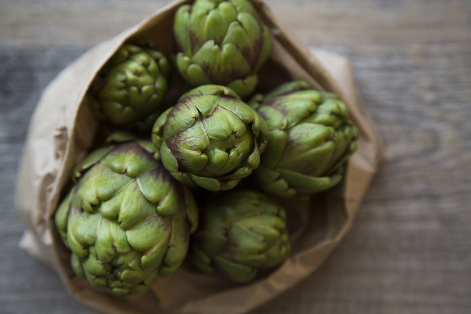 artichokes in brown paper bag on wood surface