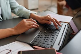 A person typing on a laptop keyboard at a desk with office supplies nearby