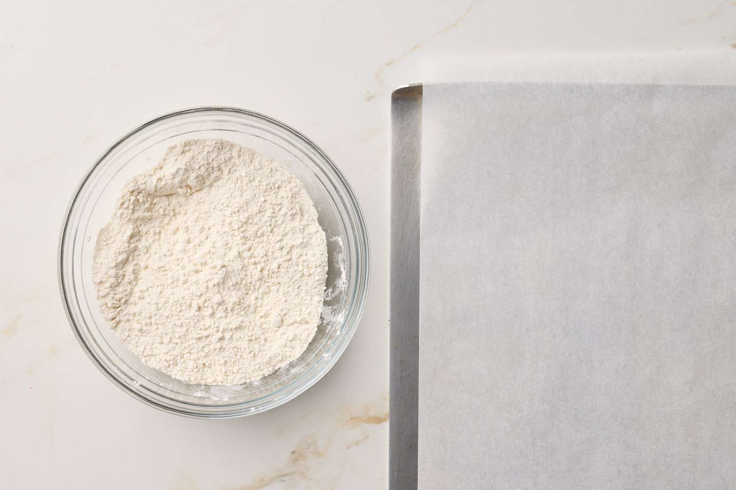 A bowl of flour next to a baking sheet lined with parchment paper