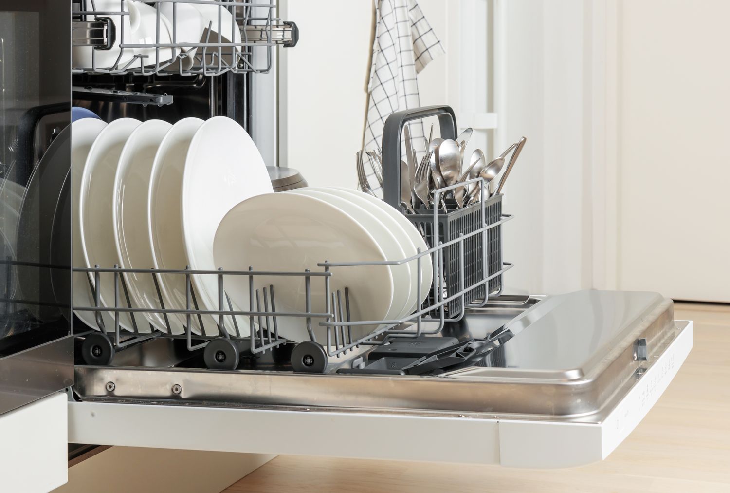 An open dishwasher with clean plates and utensils loaded in the racks