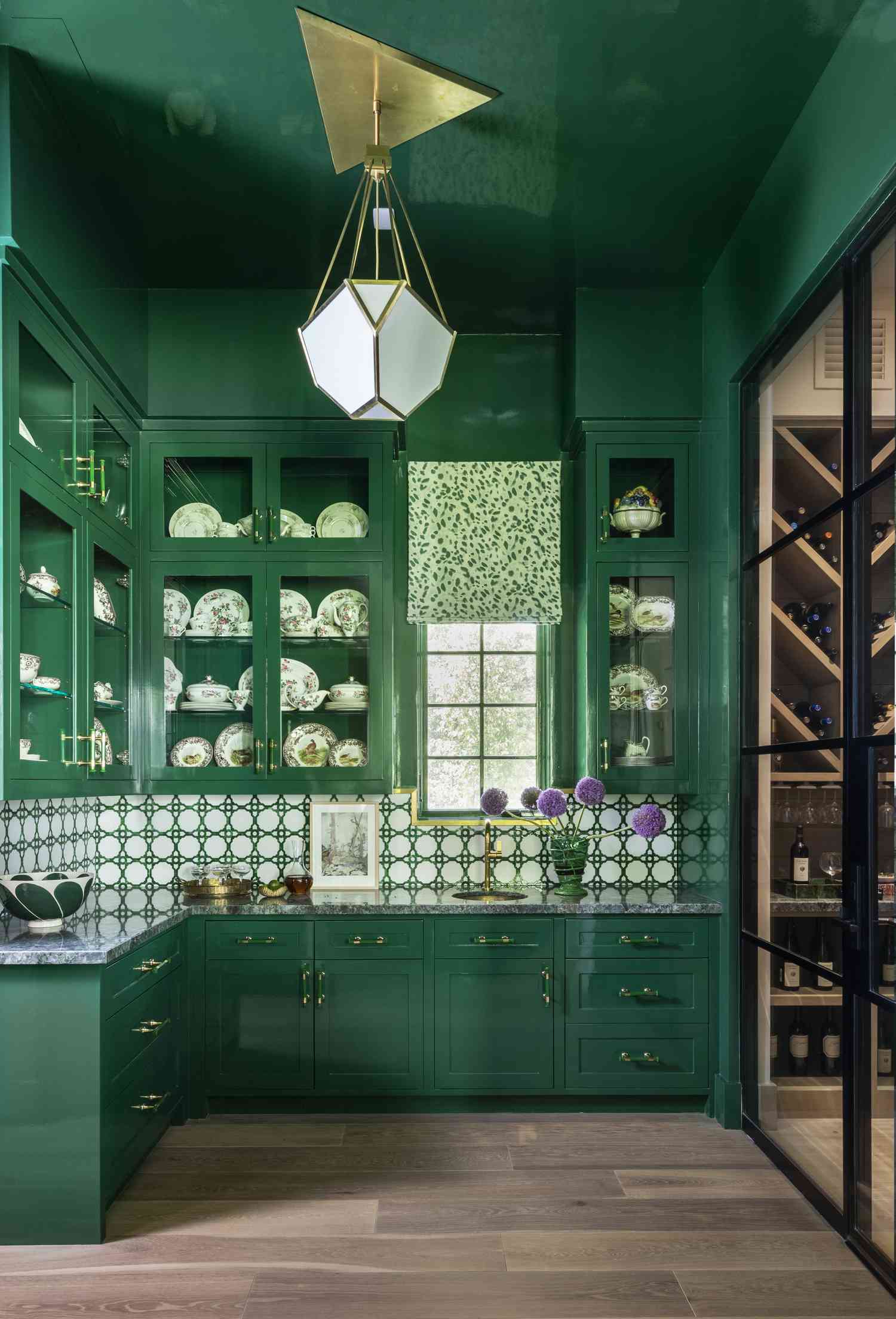 Kitchen design by Creative Tonic Design | Photography by Julie Soefer: lacquered emerald green cabinetry, brass hardware, patterned tile backsplash, and a striking geometric pendant light.