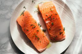Two uncooked salmon fillets garnished with herbs and placed on a plate